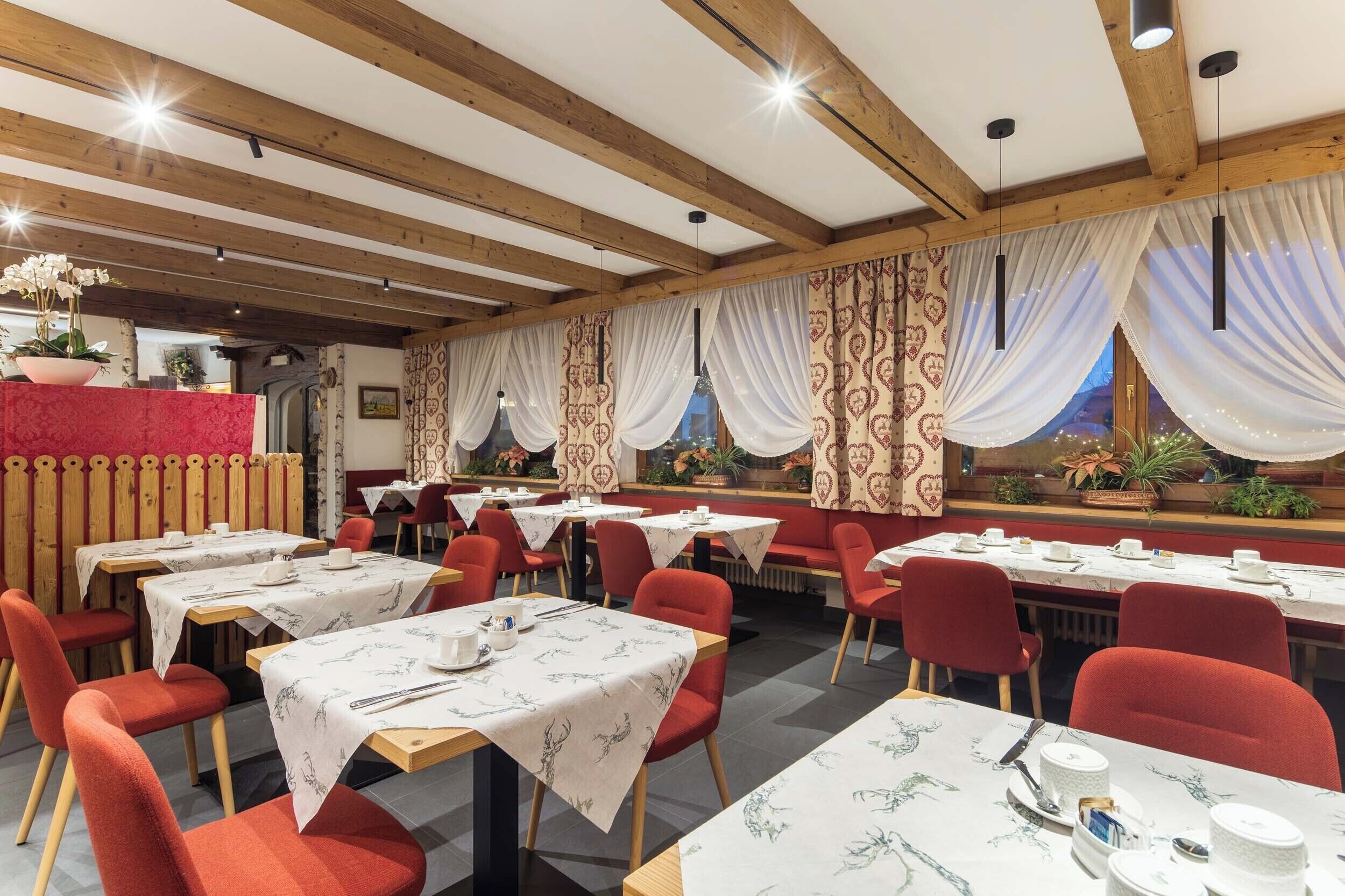 En restaurant med træbjælker, røde stole og borde dækket med hvide dugge.