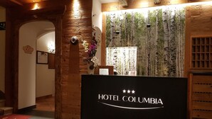 Zona de recepción con decoración de madera, un mostrador de recepción y una pared con un mural de temática natural.