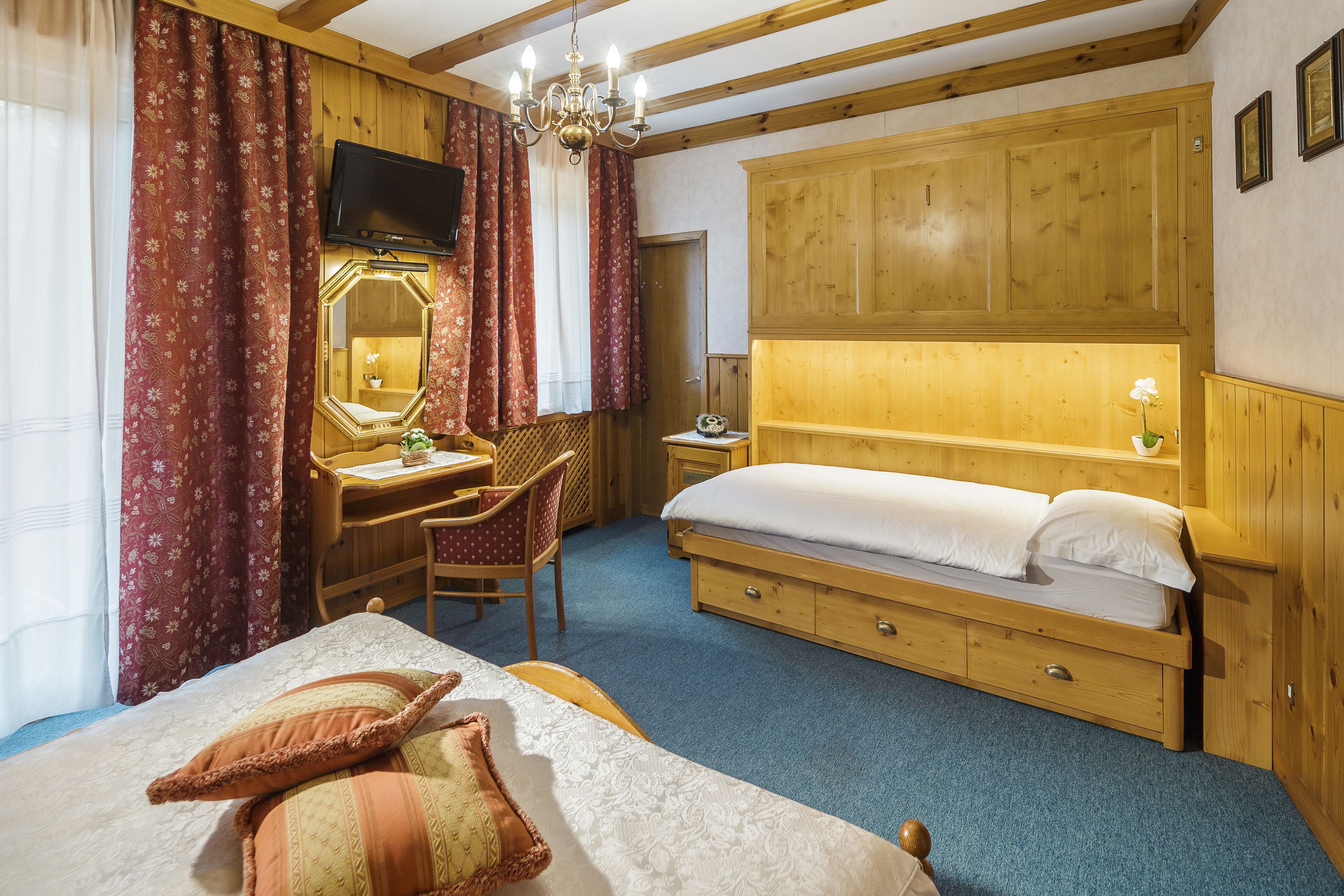 Een slaapkamer met een bed, een bureau met stoel, een spiegel, een televisie en houten lambrisering.