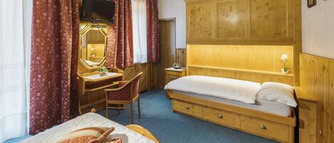 Een slaapkamer met een bed, een bureau met stoel, een spiegel, een televisie en houten lambrisering.