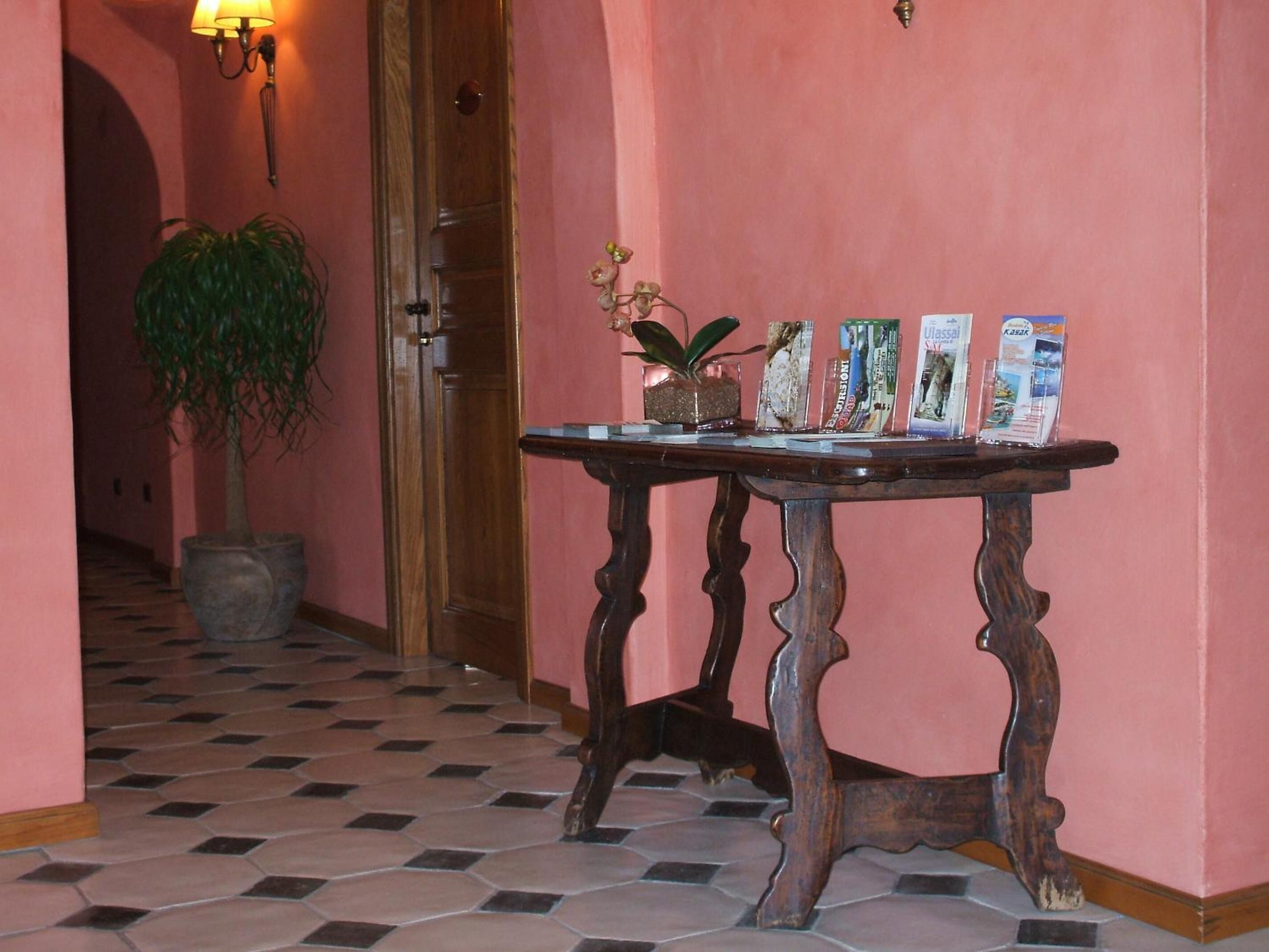 Un couloir avec un sol carrelé, une porte en bois, une table avec des brochures et une plante en pot.