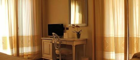 A hotel room with a desk, chair, and a bed.
