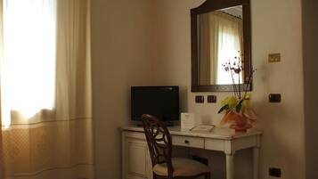 A hotel room with a desk, chair, television, mirror, and a vase with flowers.