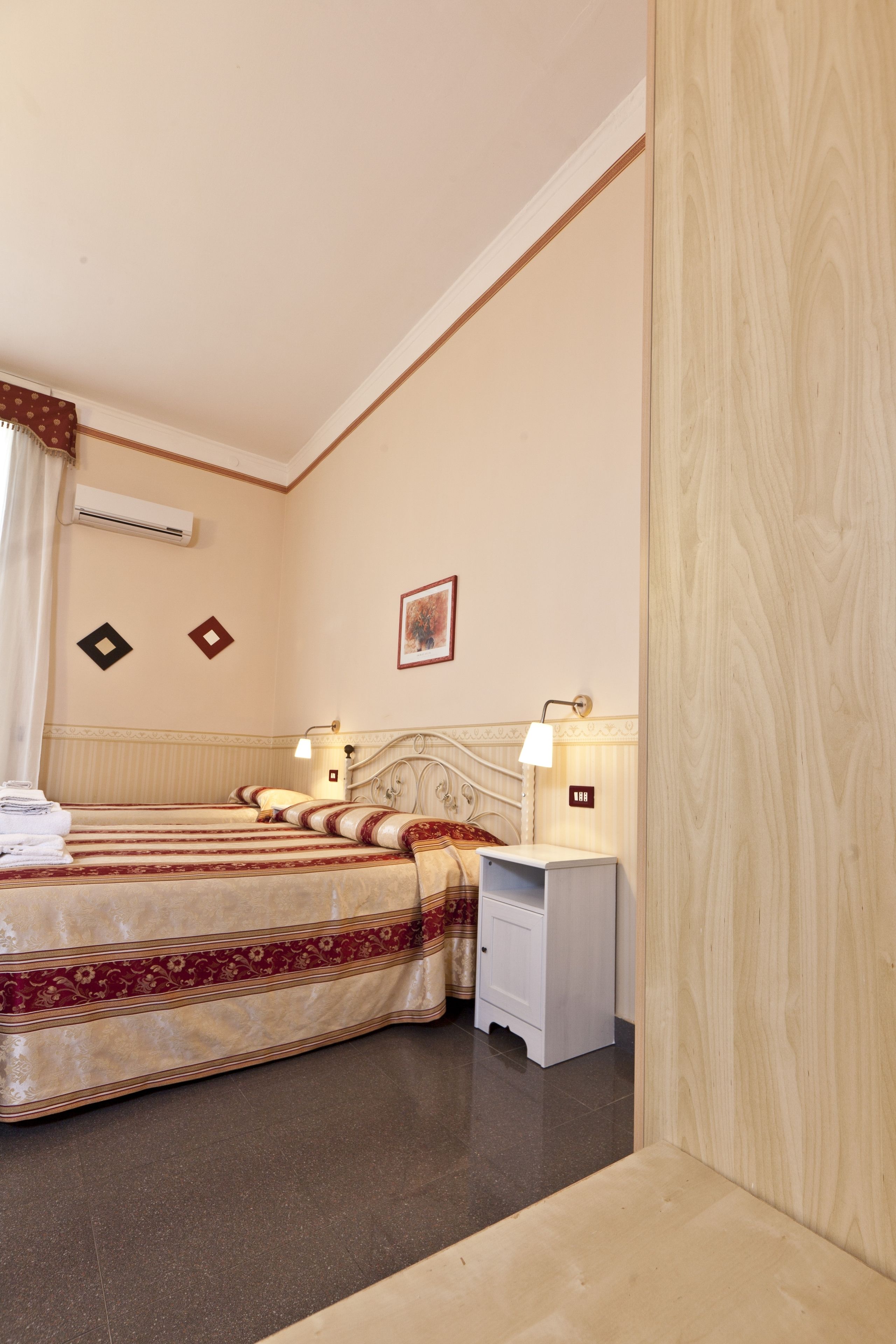 Habitación de hotel con dos camas, una mesita de noche, una lámpara y aire acondicionado instalado en la pared.