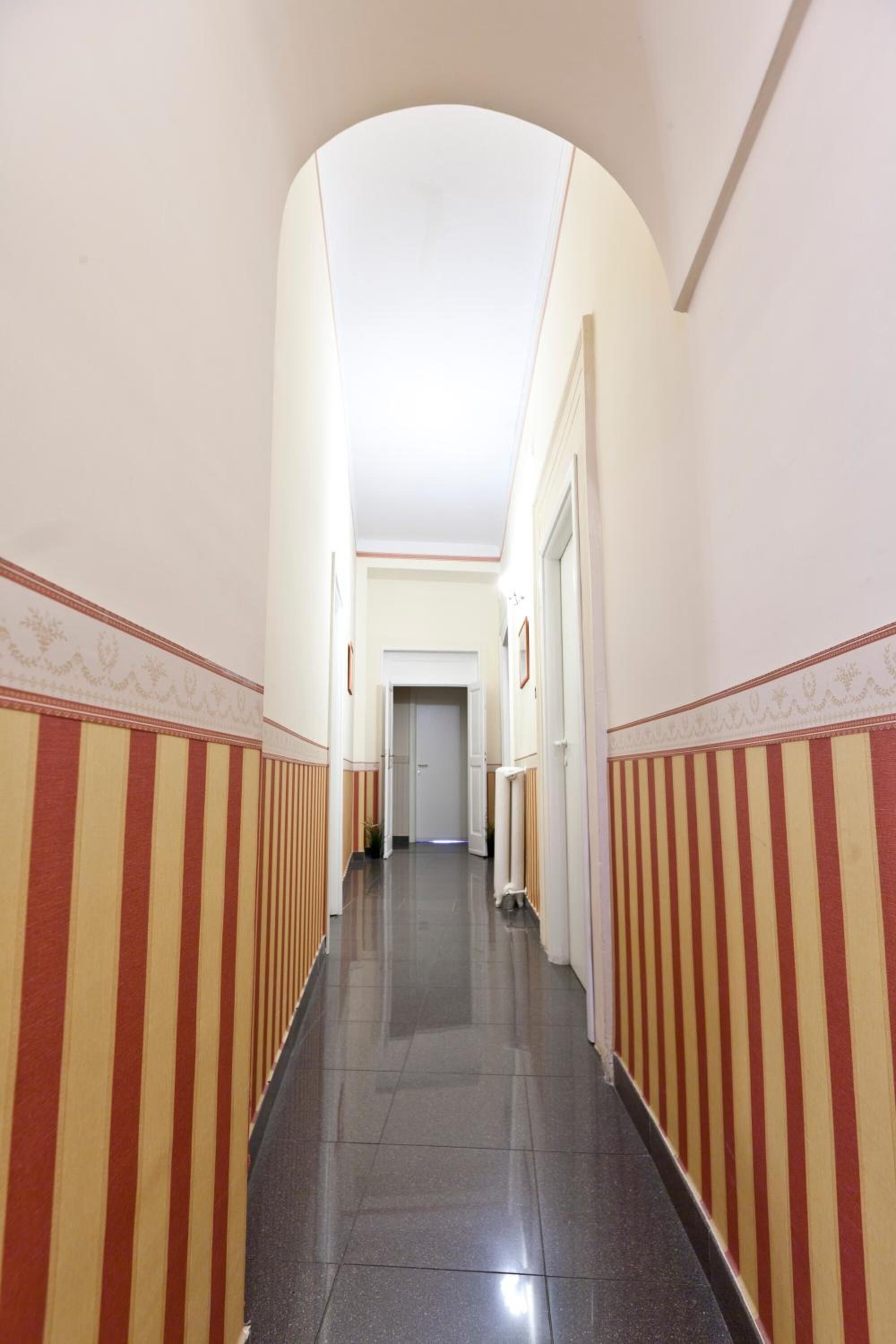A hallway with striped walls and a tiled floor, leading to a door at the end.