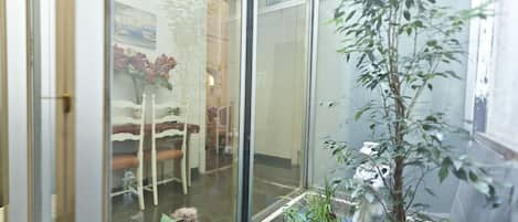 Una habitación con una puerta de vidrio que da a un comedor, una planta en maceta y una pequeña mesa con sillas.