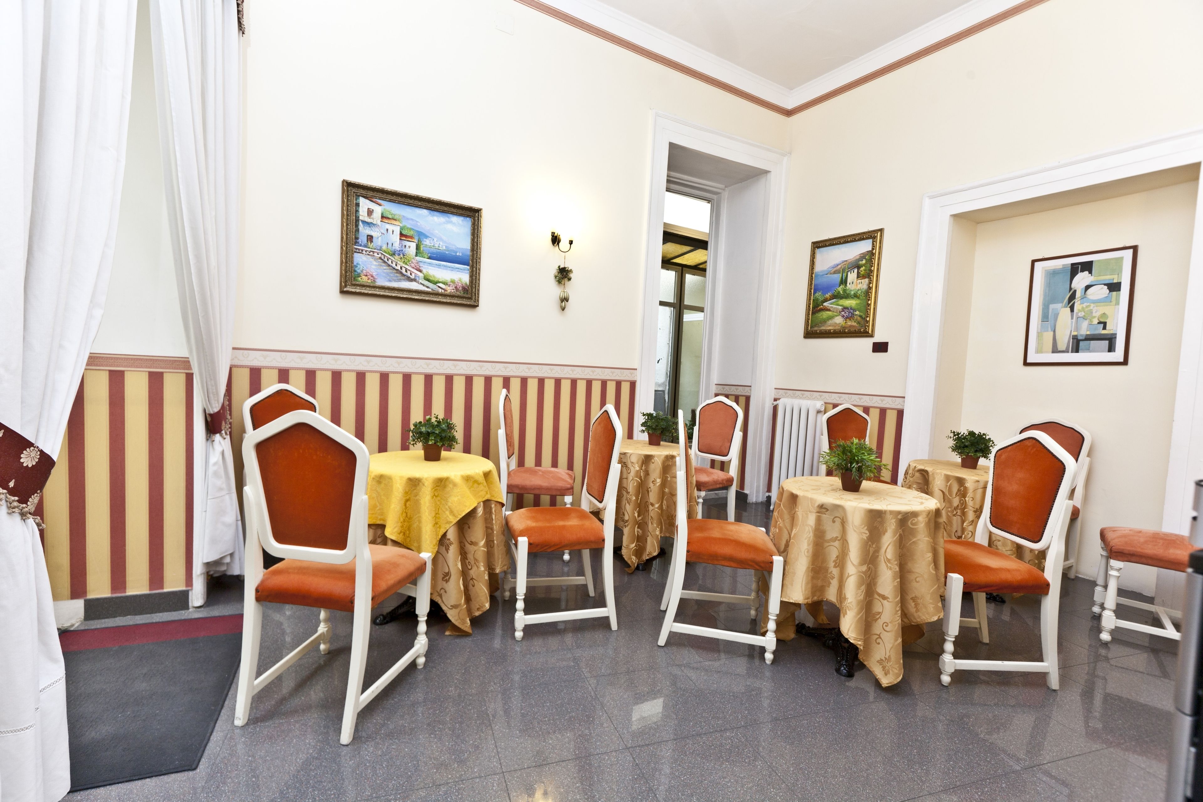 A dining area with striped walls, multiple tables with yellow tablecloths, and orange chairs.