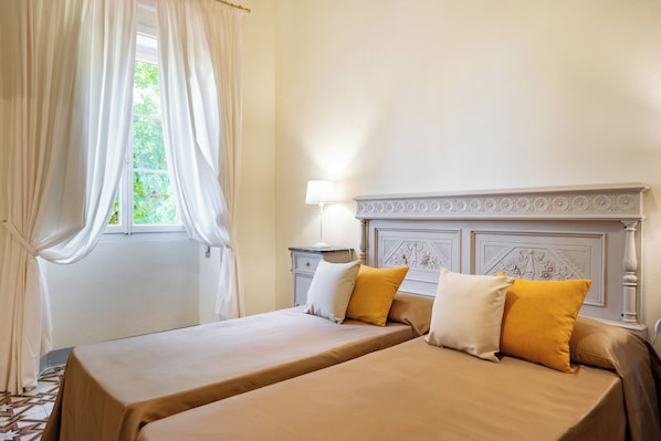 A double bed with two pillows, a nightstand with a lamp, and a window with curtains.