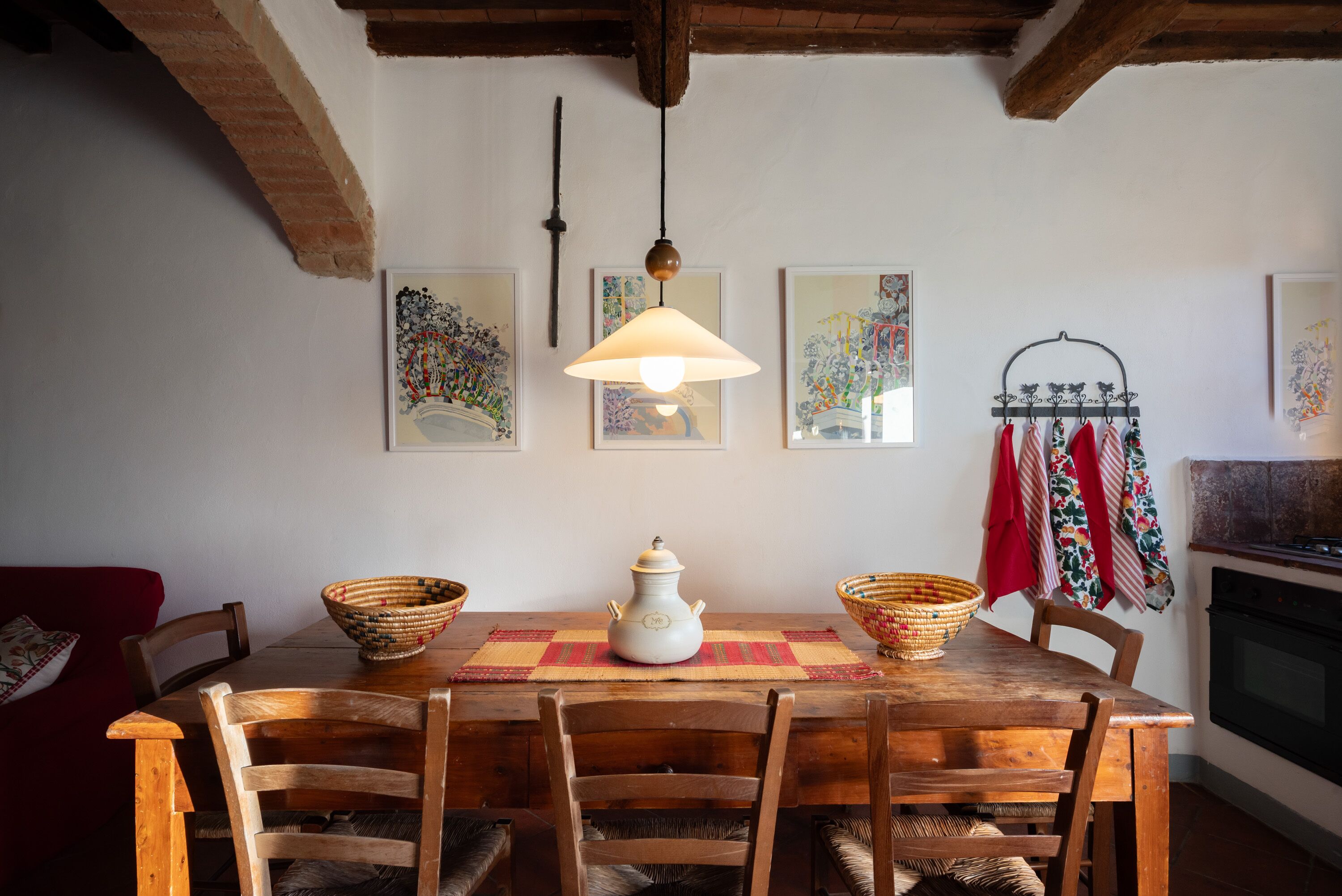 Una mesa de madera con sillas, una lámpara colgante y obras de arte en la pared.