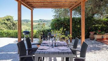 An outdoor dining area with a pergola, a table set for six, and a scenic view of hills and greenery.