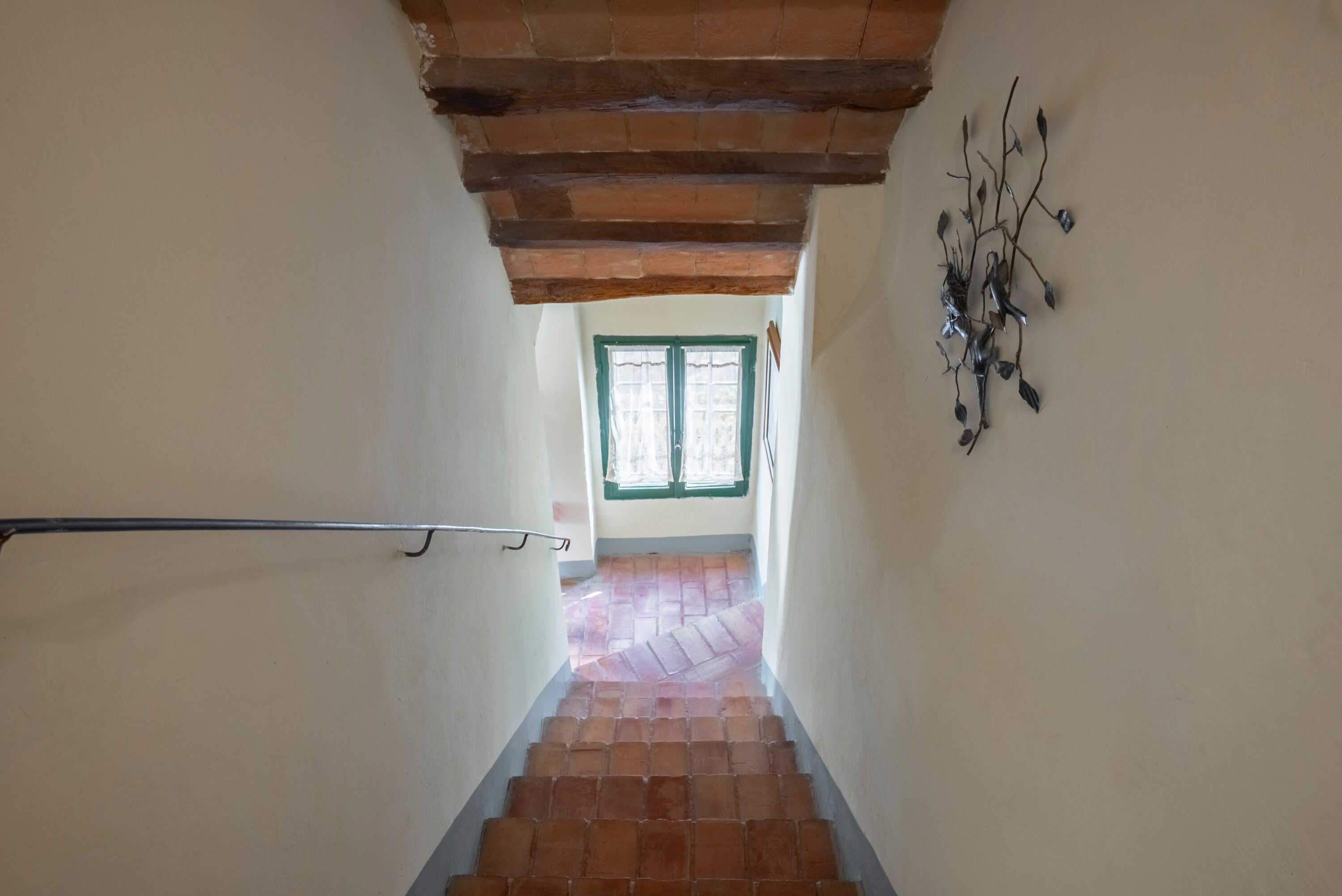 Una escalera con barandilla metálica, un adorno de pared de metal y una ventana con detalles en verde en la parte superior.