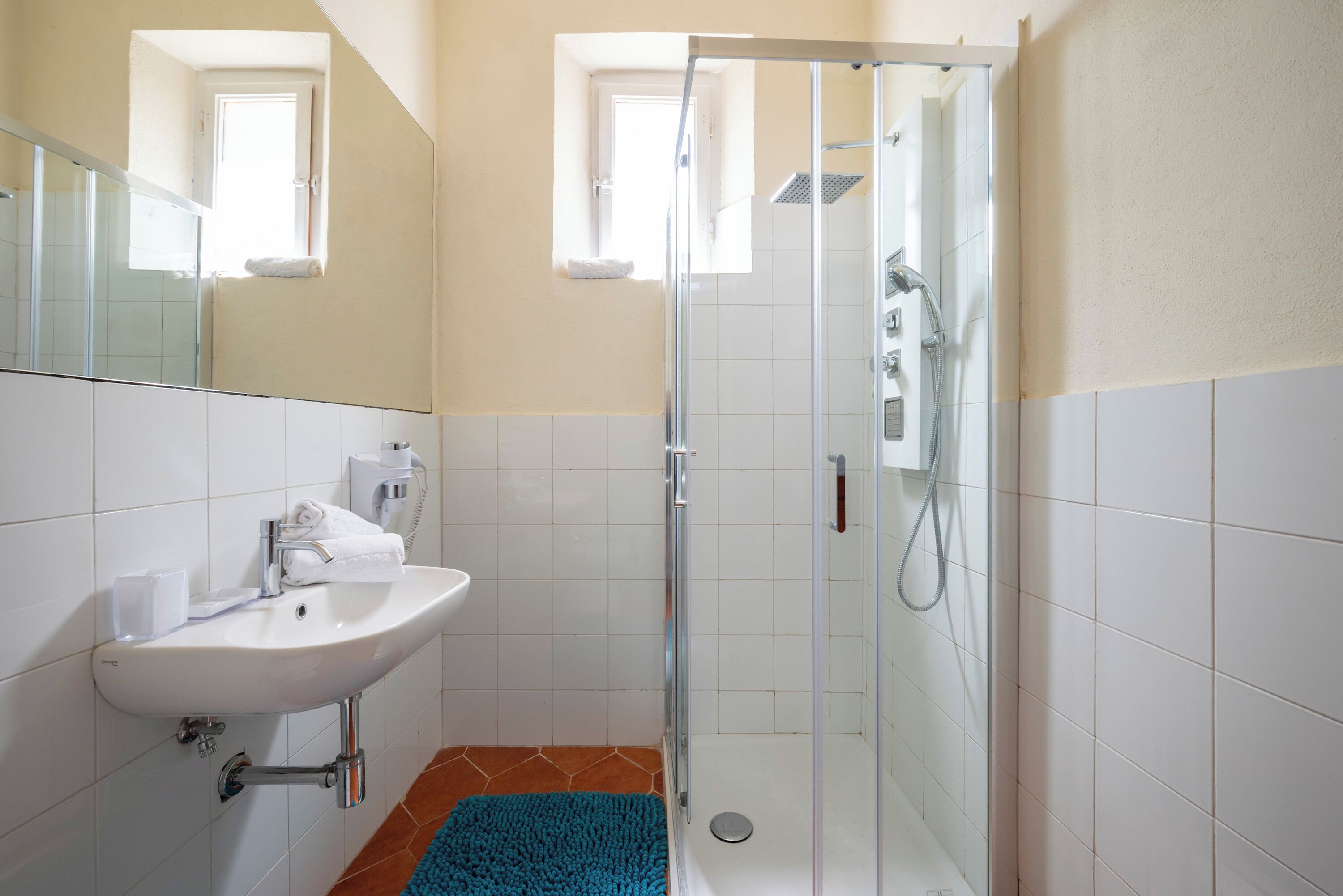 A bathroom with a sink, mirror, shower, and a blue rug.
