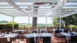 An outdoor dining area with tables set for two, surrounded by a pergola structure, overlooking a scenic landscape. - Agriturismo Bio Fattoria Bacio (Certaldo)