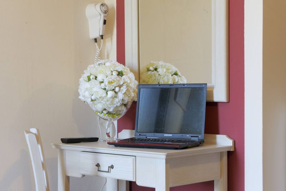 A laptop on a desk with a hairdryer and a vase of flowers.
