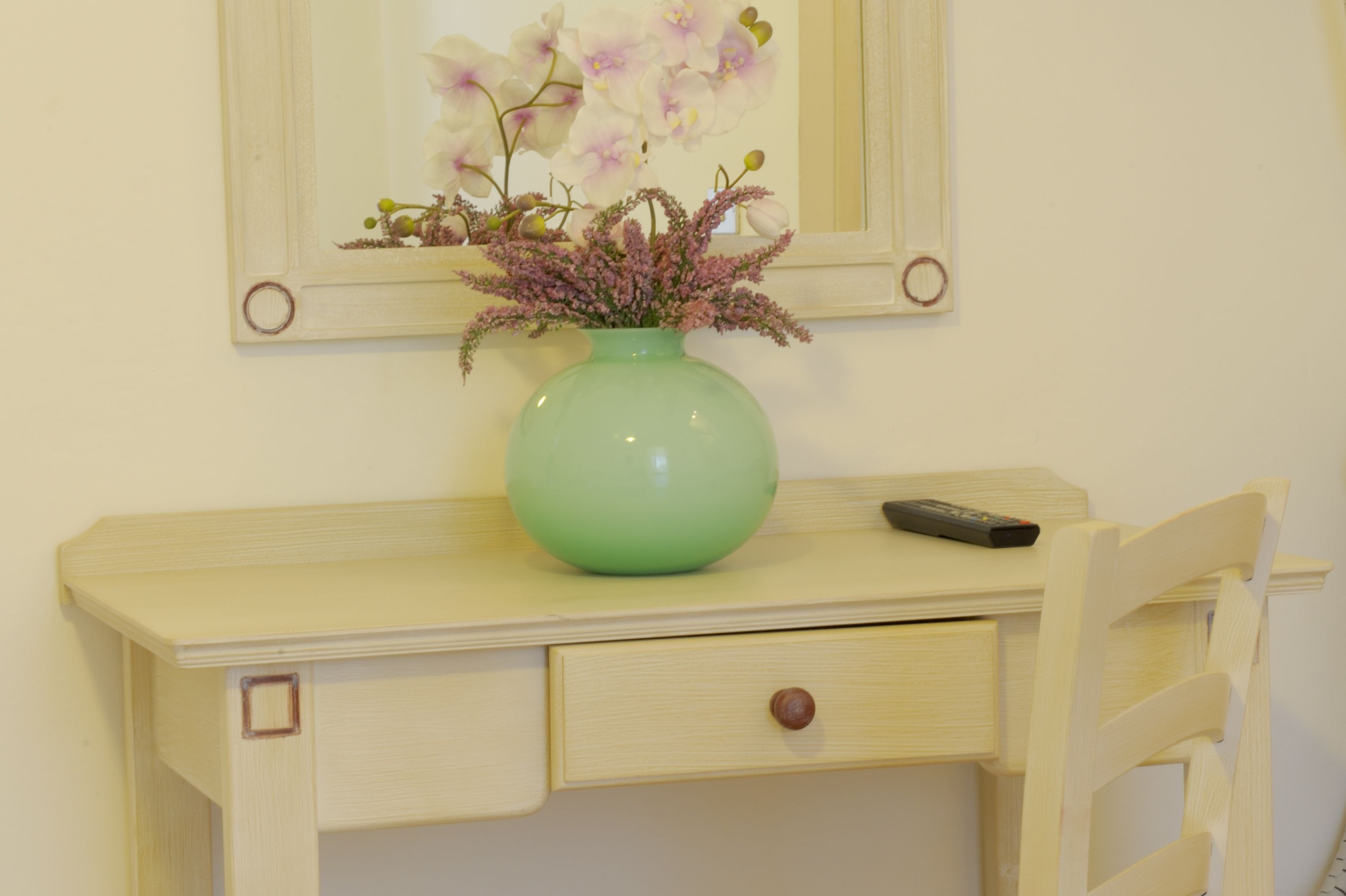 A desk with a green vase containing flowers, a remote control, and a drawer.