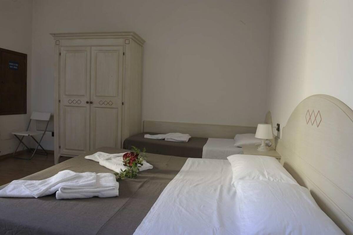 A hotel room with two beds, a wardrobe, a chair, and a desk with a lamp.