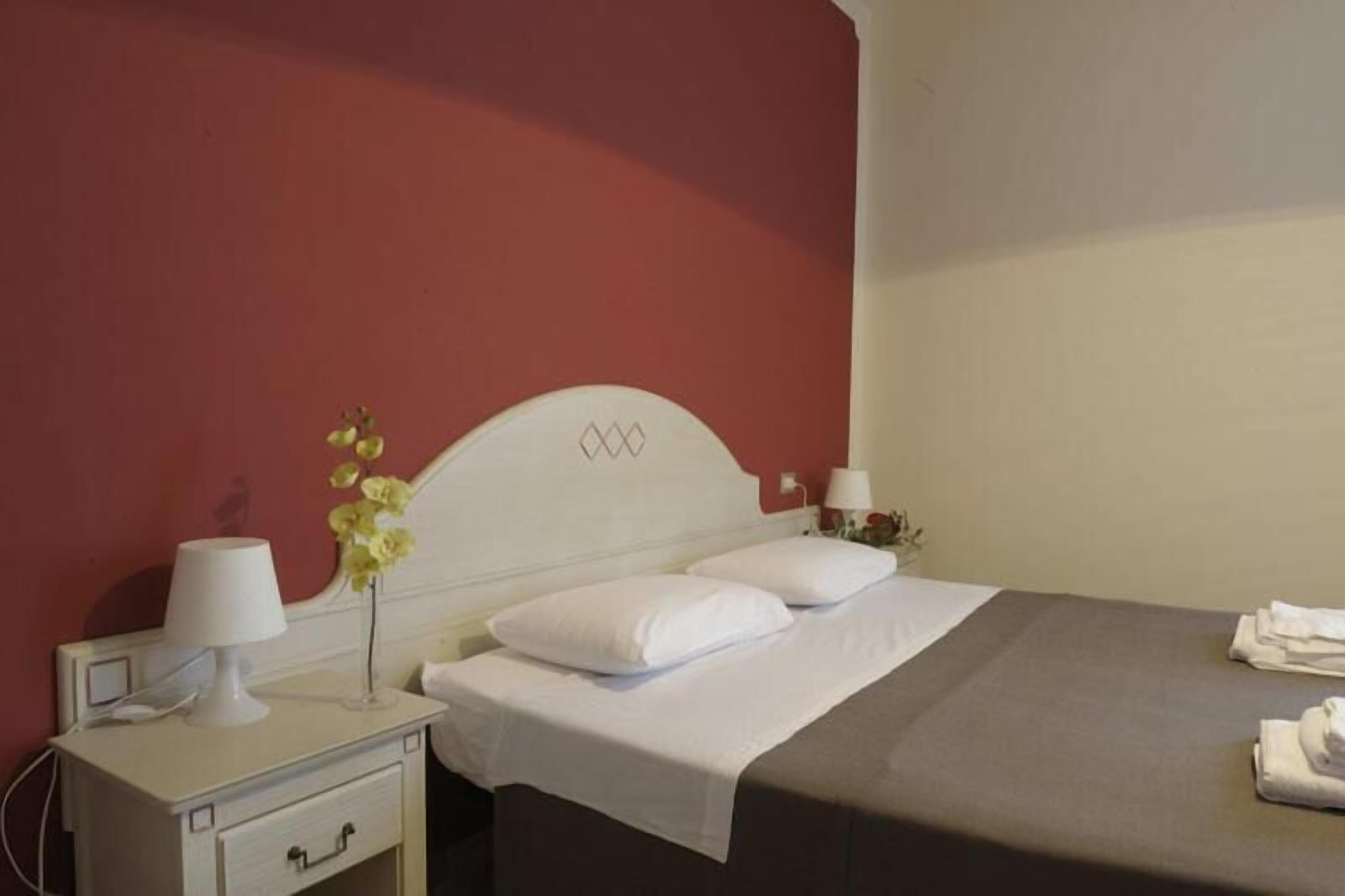 Une chambre d’hôtel avec un lit, une table de chevet avec une lampe, un vase de fleurs et une commode avec un tiroir.