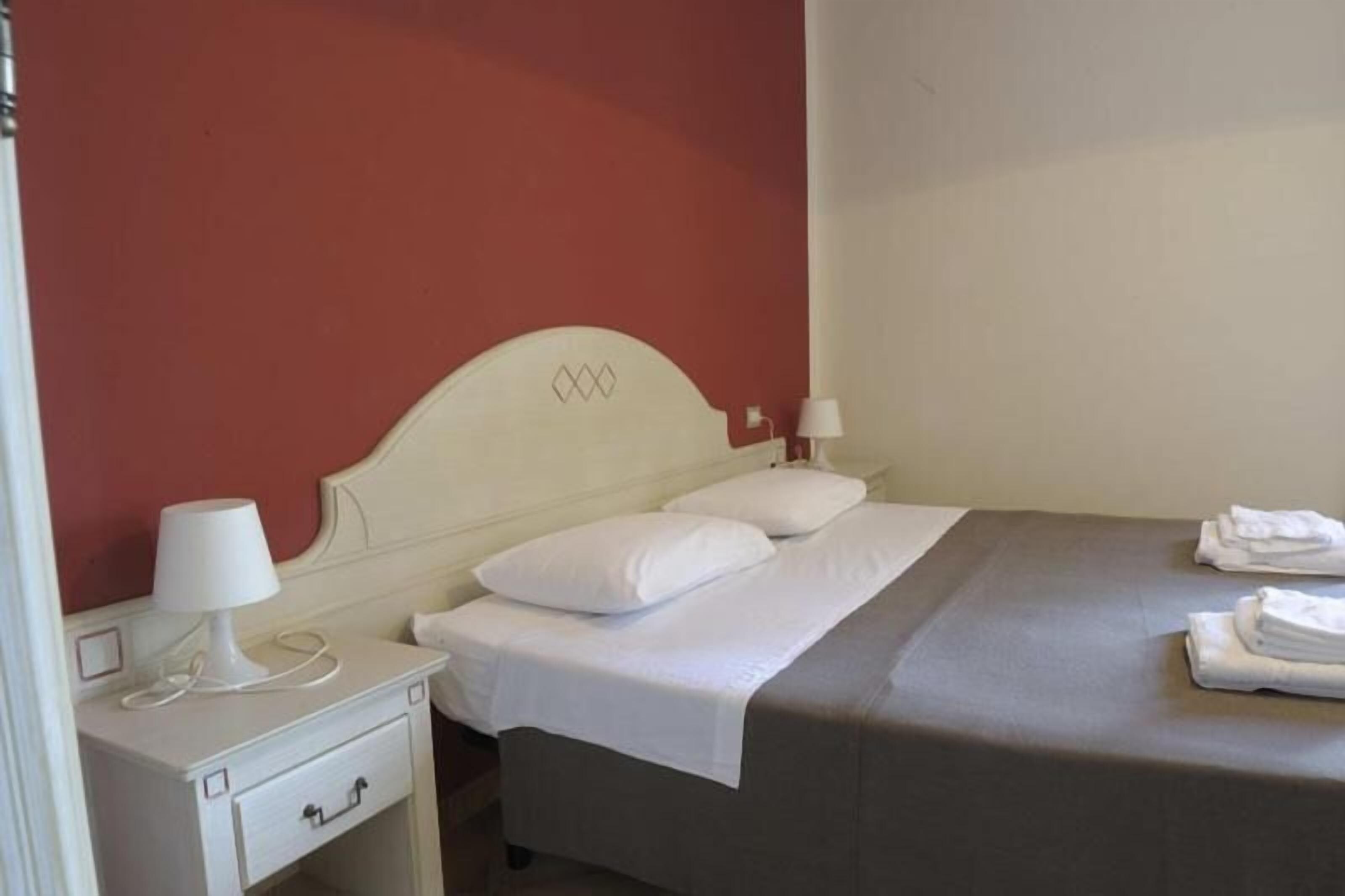 A neatly made bed with white linens and pillows, a bedside table with a lamp, and a folded towel on the bed.