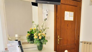 A room with a desk, a chair, a television mounted above the desk, a wooden door, and a small vase with flowers. - La Spiga (Campi Bisenzio)
