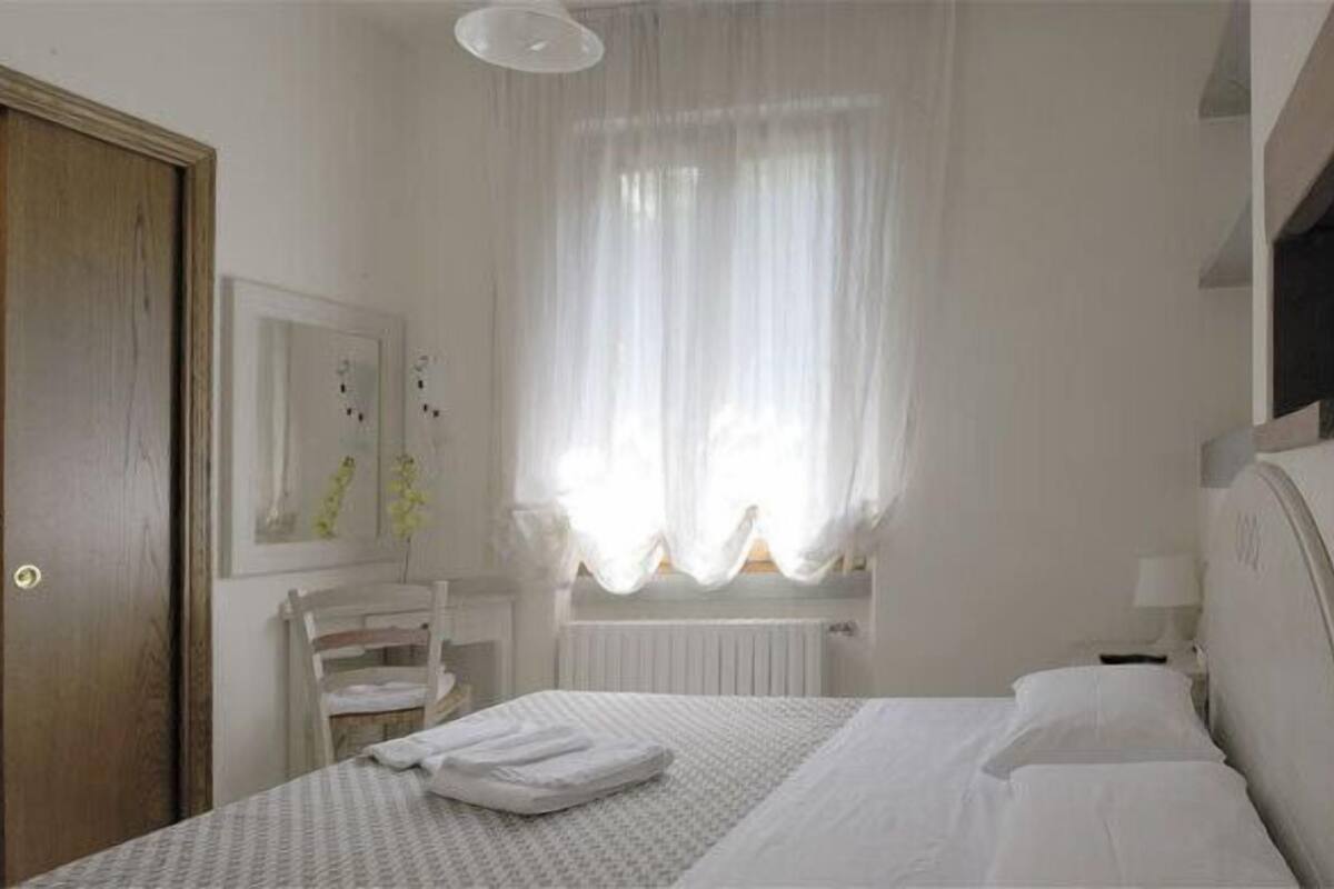 A bedroom with a bed, a chair, a window with curtains, a radiator, and a door.