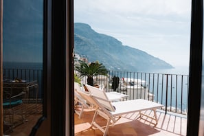 A balcony with white lounge chairs, a small table, and a potted plant. - Villa Principe Giovanni (Positano)
