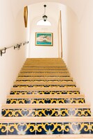 A staircase with ornate yellow and blue tiles, a hanging light fixture, and a framed picture on the wall.