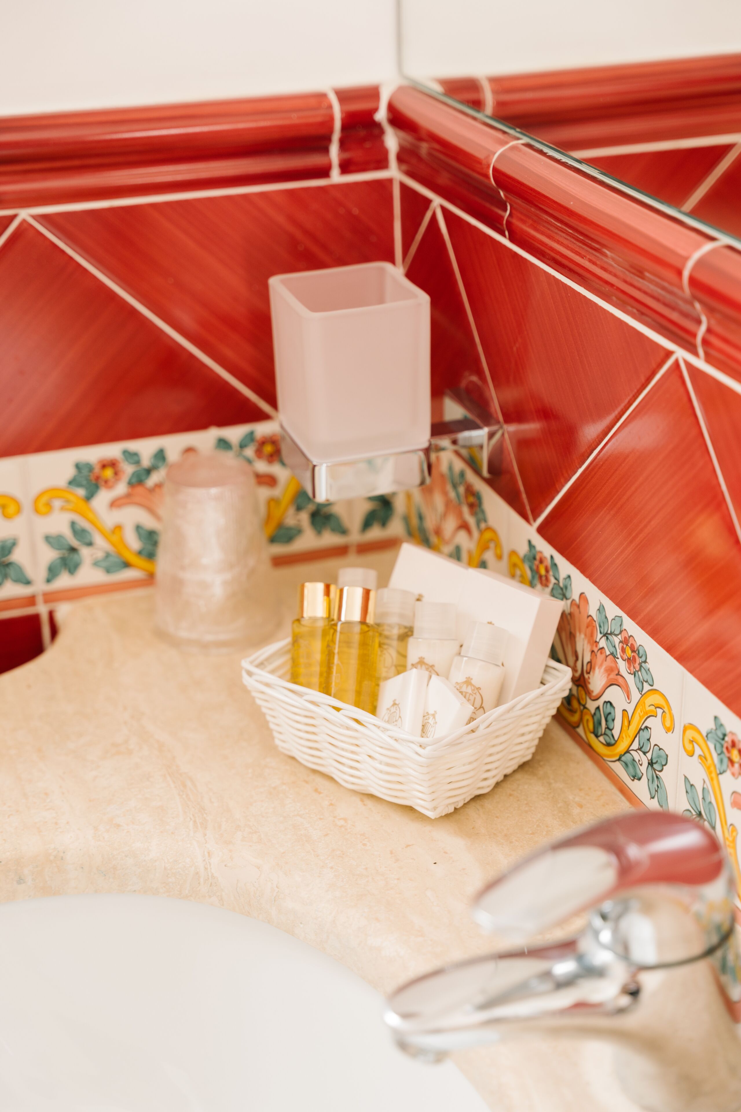 A bathroom with a red tiled shower enclosure, a white sink, and a basket of toiletries.