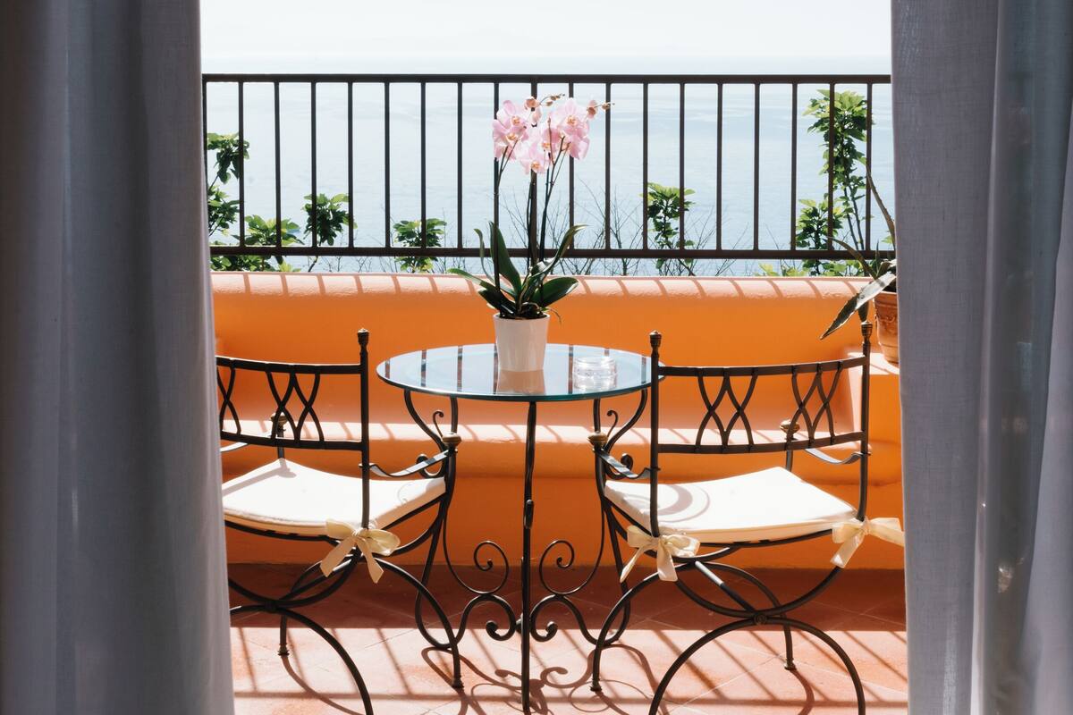 Un balcon avec une table et des chaises, une plante en pot et une vue sur la mer.