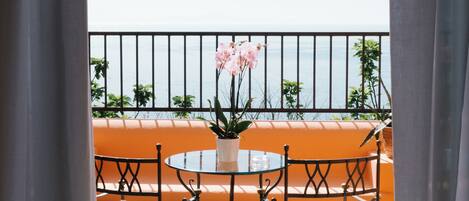 A balcony with a table and chairs, a potted plant, and a view of the sea.