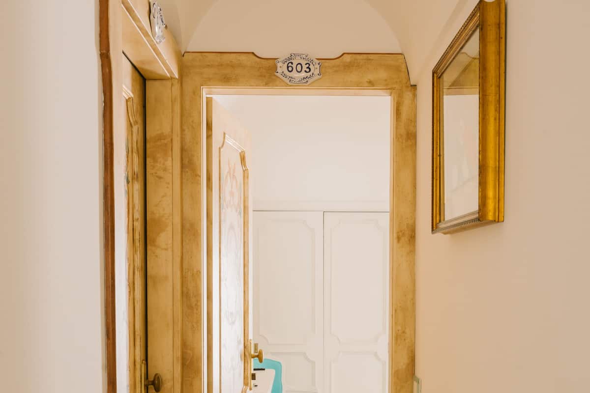 Un couloir étroit, dont le sol est recouvert de carreaux, mène à une pièce où se trouvent un lavabo et une chaise.