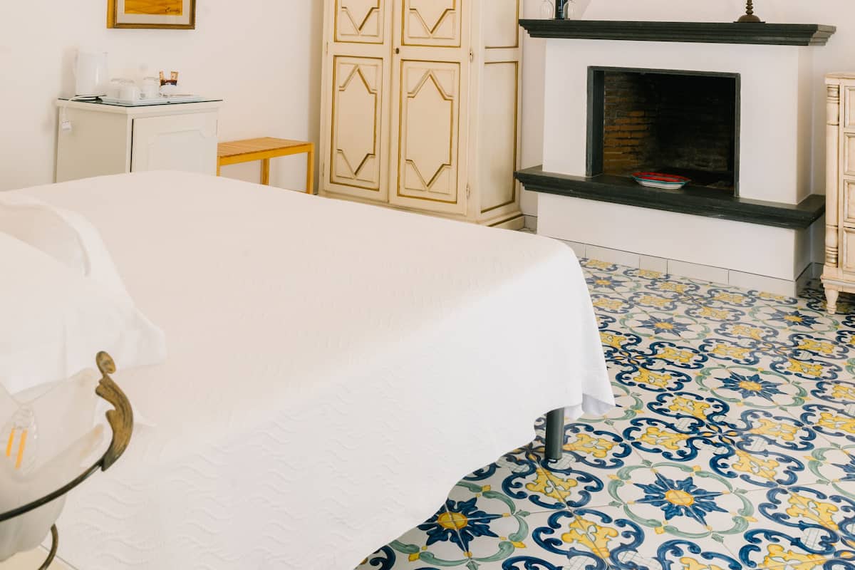 Une chambre à coucher avec un lit, un lustre, une cheminée, une armoire et un tableau au mur.