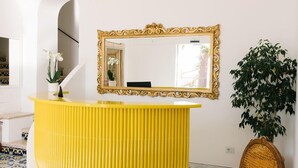 Un espace d’accueil avec un comptoir jaune, un miroir, une chaise et une plante en pot.