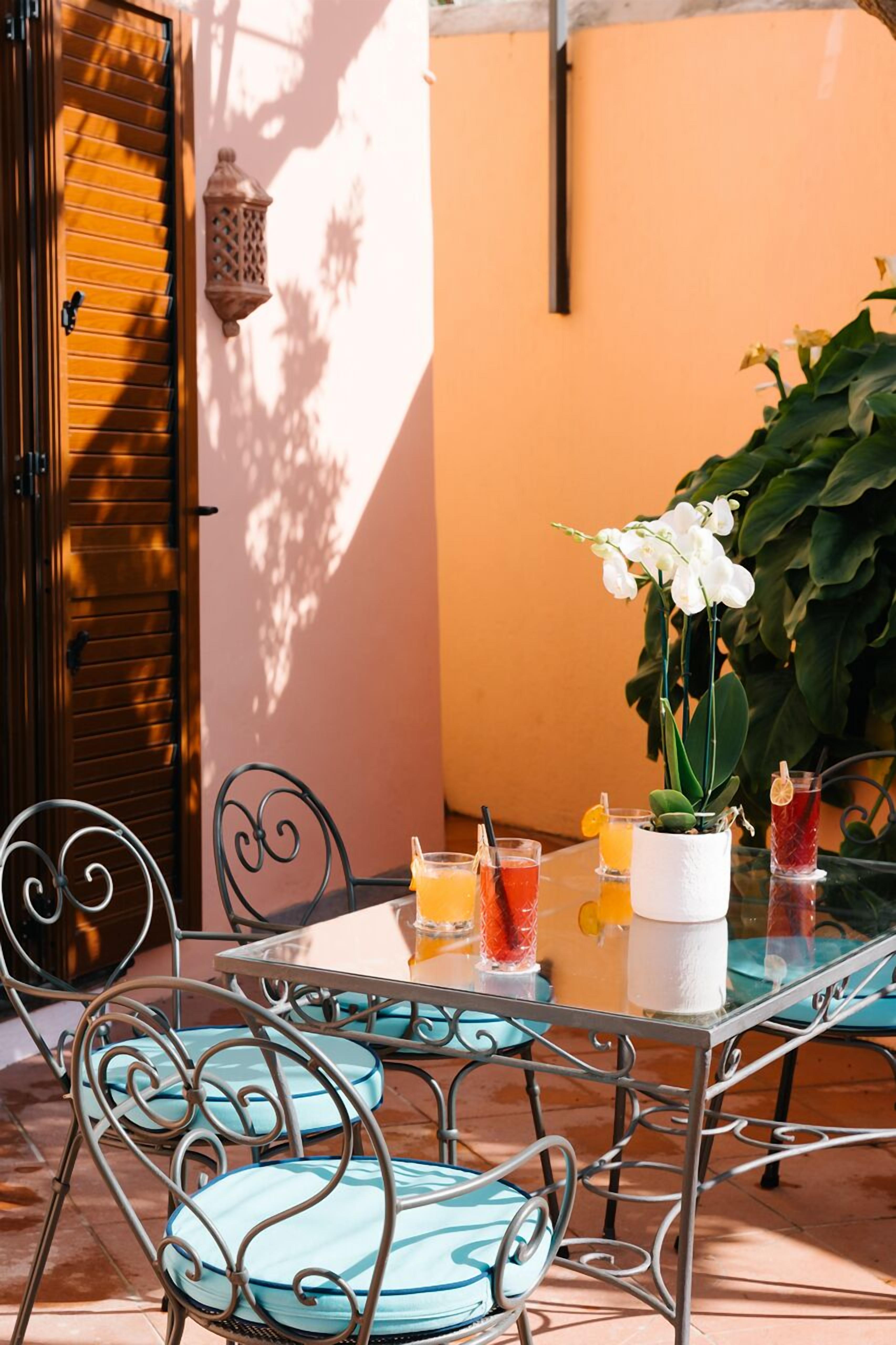 Un patio con una mesa para dos, sillas de metal y una orquídea en maceta.