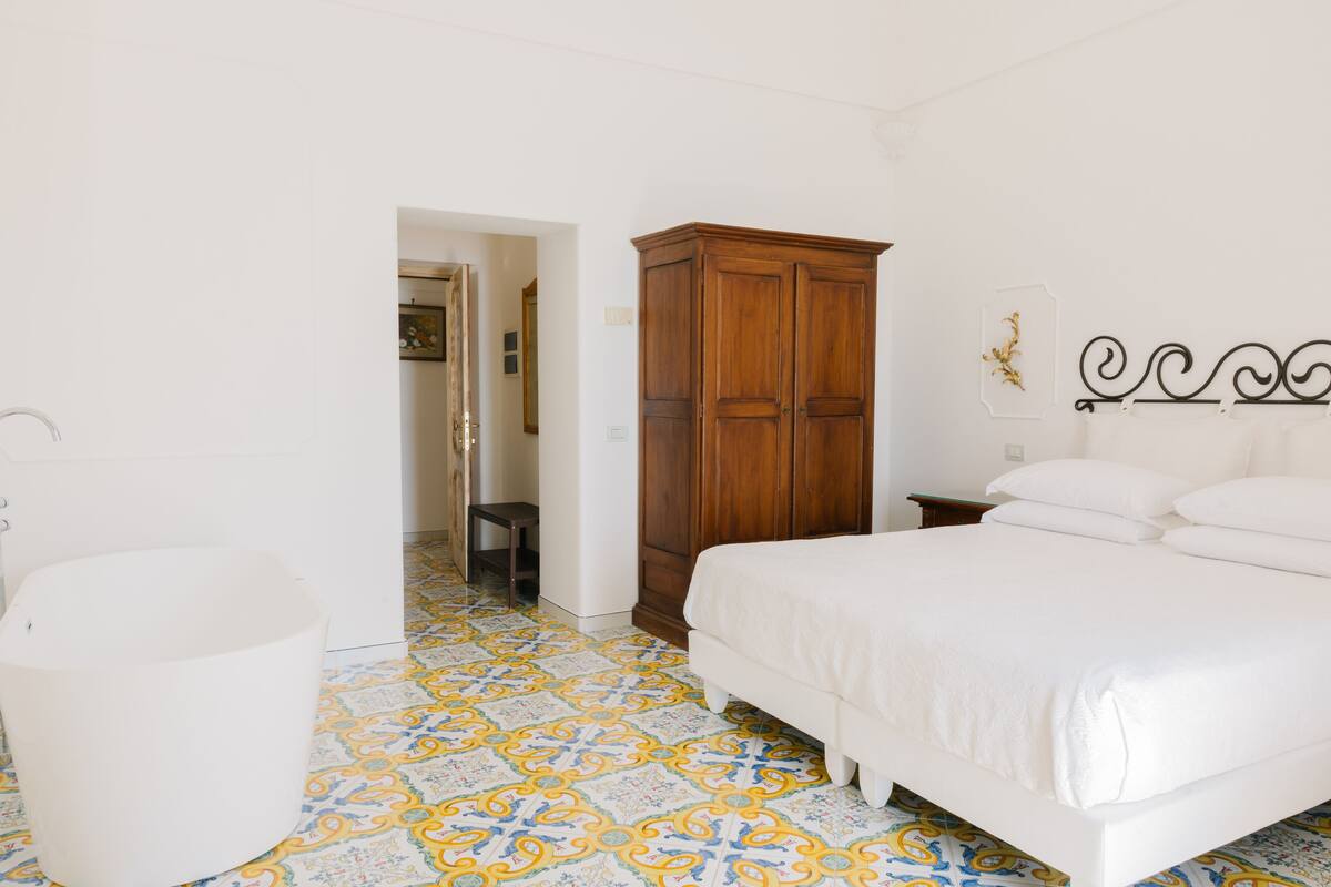 Une chambre à coucher avec un lit, une armoire en bois, une chaise blanche et des carreaux de sol à motifs.