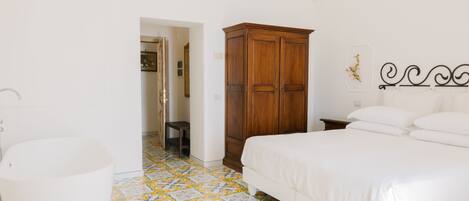 A bedroom with a bed, a wooden wardrobe, a white chair, and patterned floor tiles.