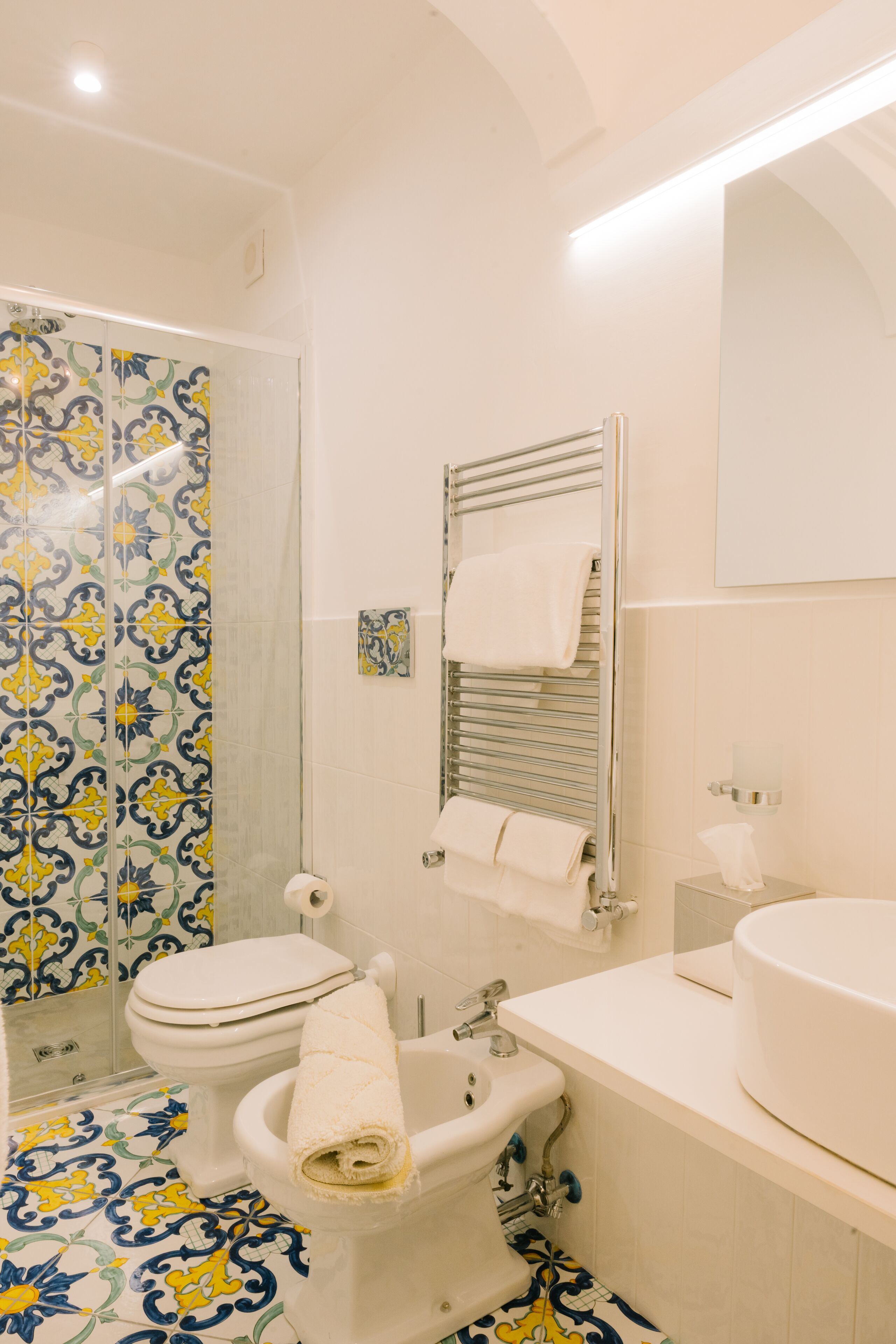 A bathroom with a toilet, bidet, sink, and a shower with patterned tiles.