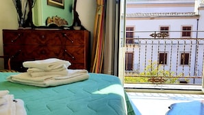 A hotel room with a bed, a dresser, a painting, and a view of a building with a dome. - Cavour il Conte Camillo Bed&Breakfast (Palermo)