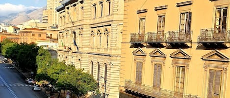 A street view with a building featuring classical architecture, a clear sky, and a road with vehicles.