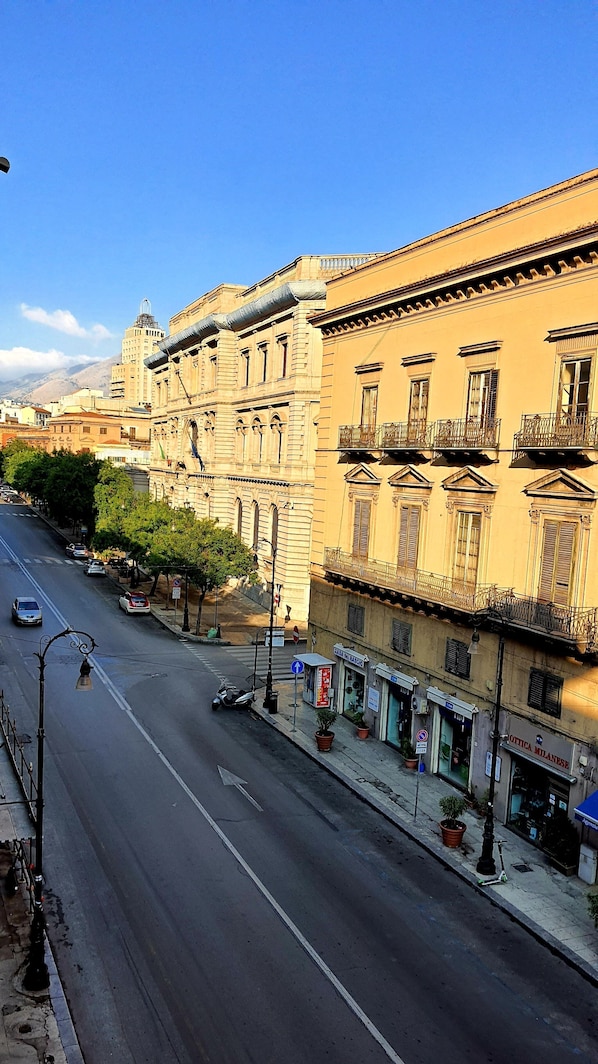 A street view with a building featuring classical architecture, a clear sky, and a road with vehicles.