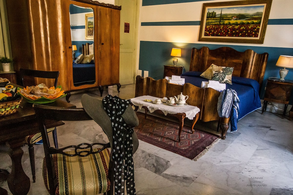 A traditional room with a wooden bed, a small table with tea set, a chair, and a decorative mirror.