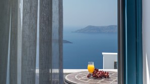 A balcony with a table set for a drink and grapes, overlooking a body of water and a distant island. - Anteliz Suites (Santorini)