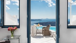 An open door leading to a balcony with a table set for breakfast, overlooking a scenic view of the sea and islands. - Anteliz Suites (Santorini)
