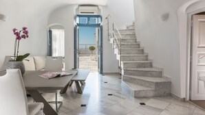 A modern interior with a marble staircase, a dining area with a table and chairs, and a view through an open door. - Anteliz Suites (Santorini)