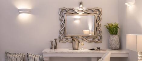 A bathroom with a marble countertop, a large mirror with an ornate frame, a vase with a plant, and two wall-mounted lights.