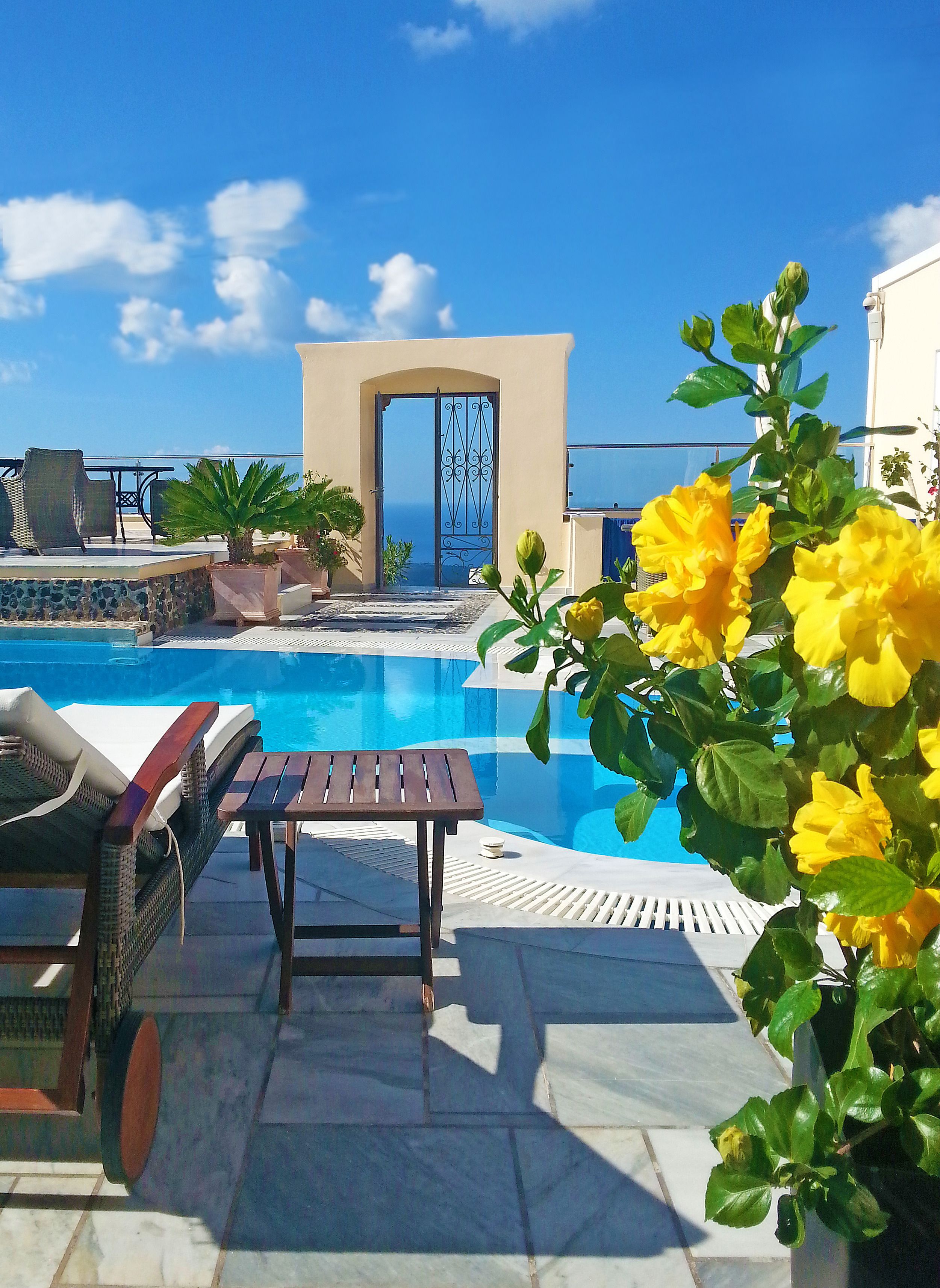 A pool area with lounge chairs and a table, a decorative archway, and a view of the sea.