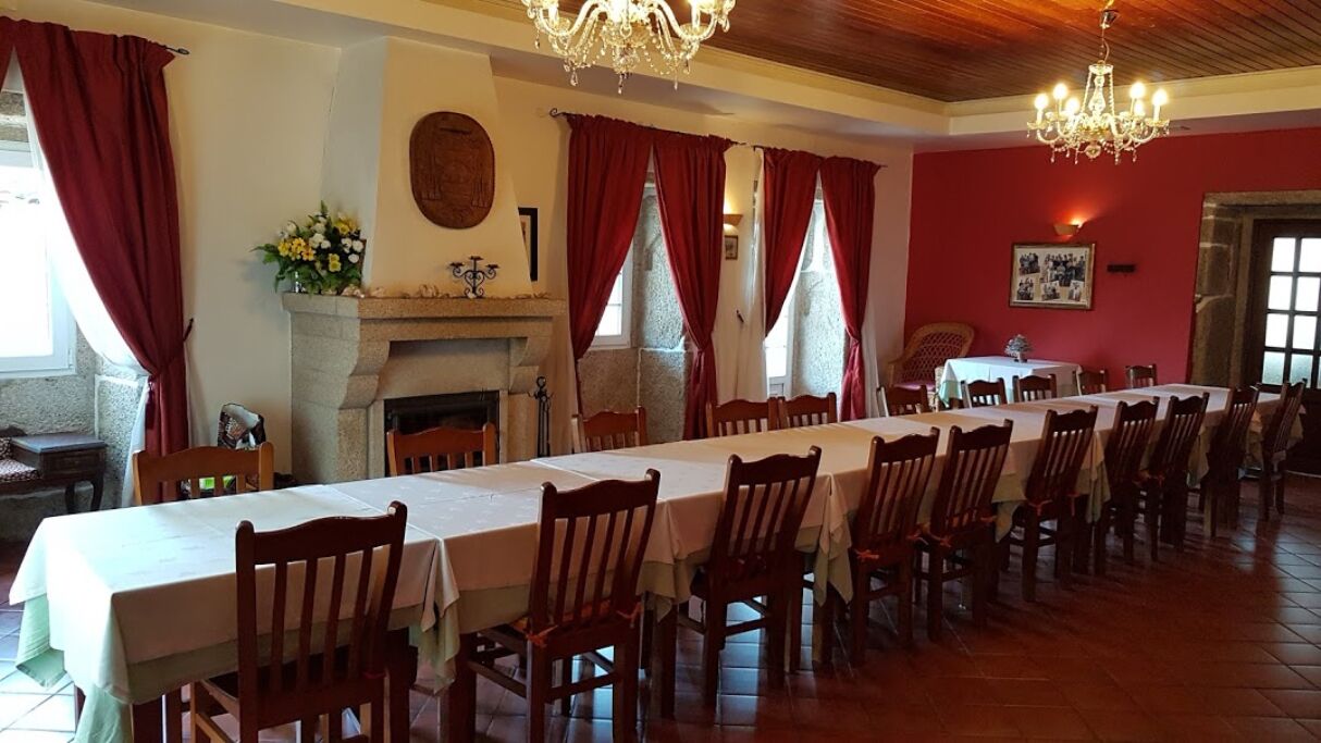 A long dining table with chairs, a fireplace, and red curtains.