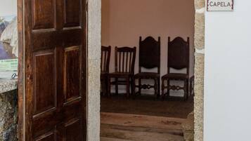 Un vano de puerta que da a una habitación con pared de piedra y puerta de madera. Hay tres sillas de madera en la habitación.