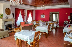 A dining area with multiple tables and chairs, a fireplace, and red curtains.