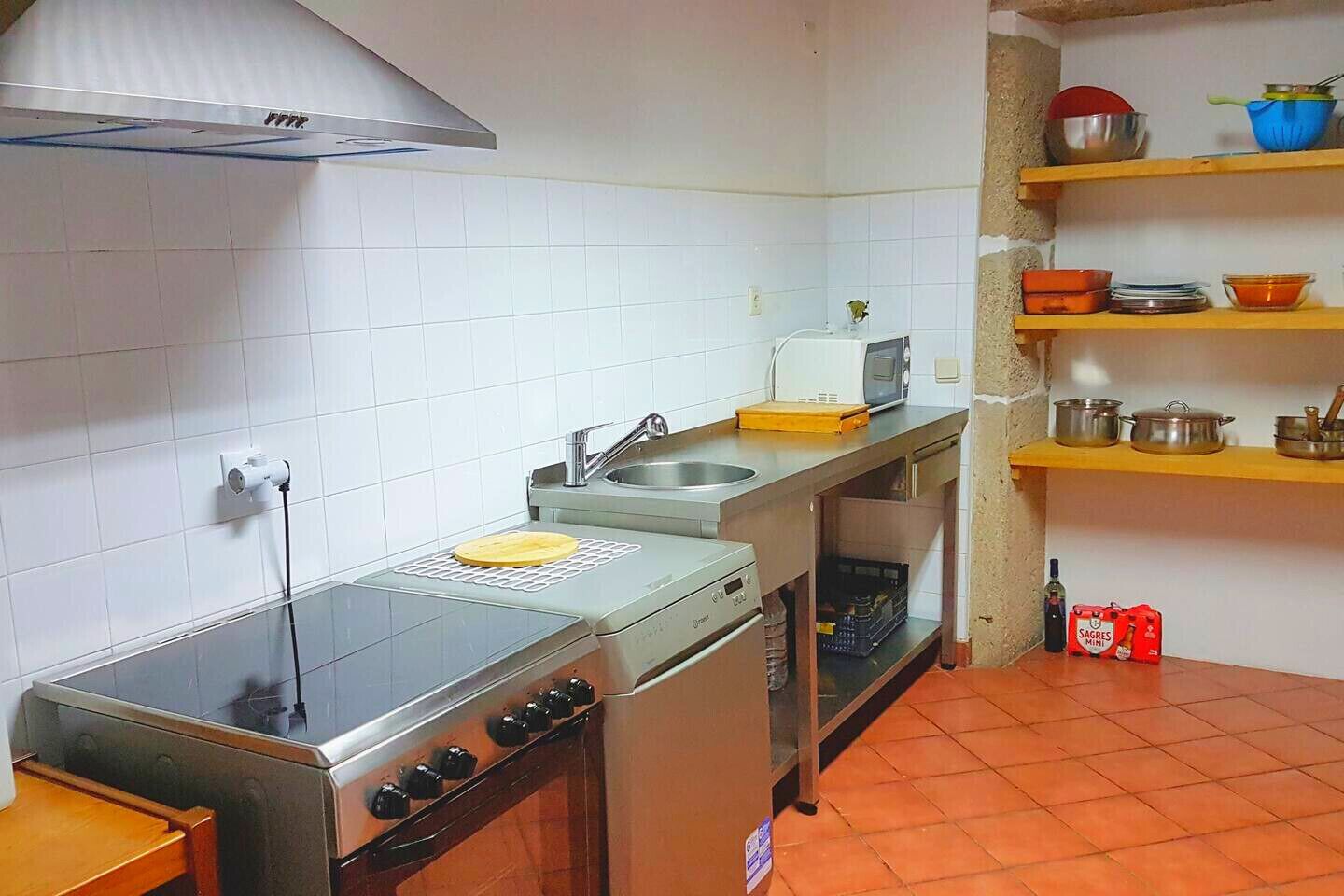 A compact kitchen with a gas stove, microwave, and oven. There are shelves with kitchenware and a bottle of wine on the counter.