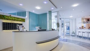 A reception area with a curved counter, a sign reading "Schillerpark," and a modern interior design. - Hotel am Schillerpark (Esslingen)